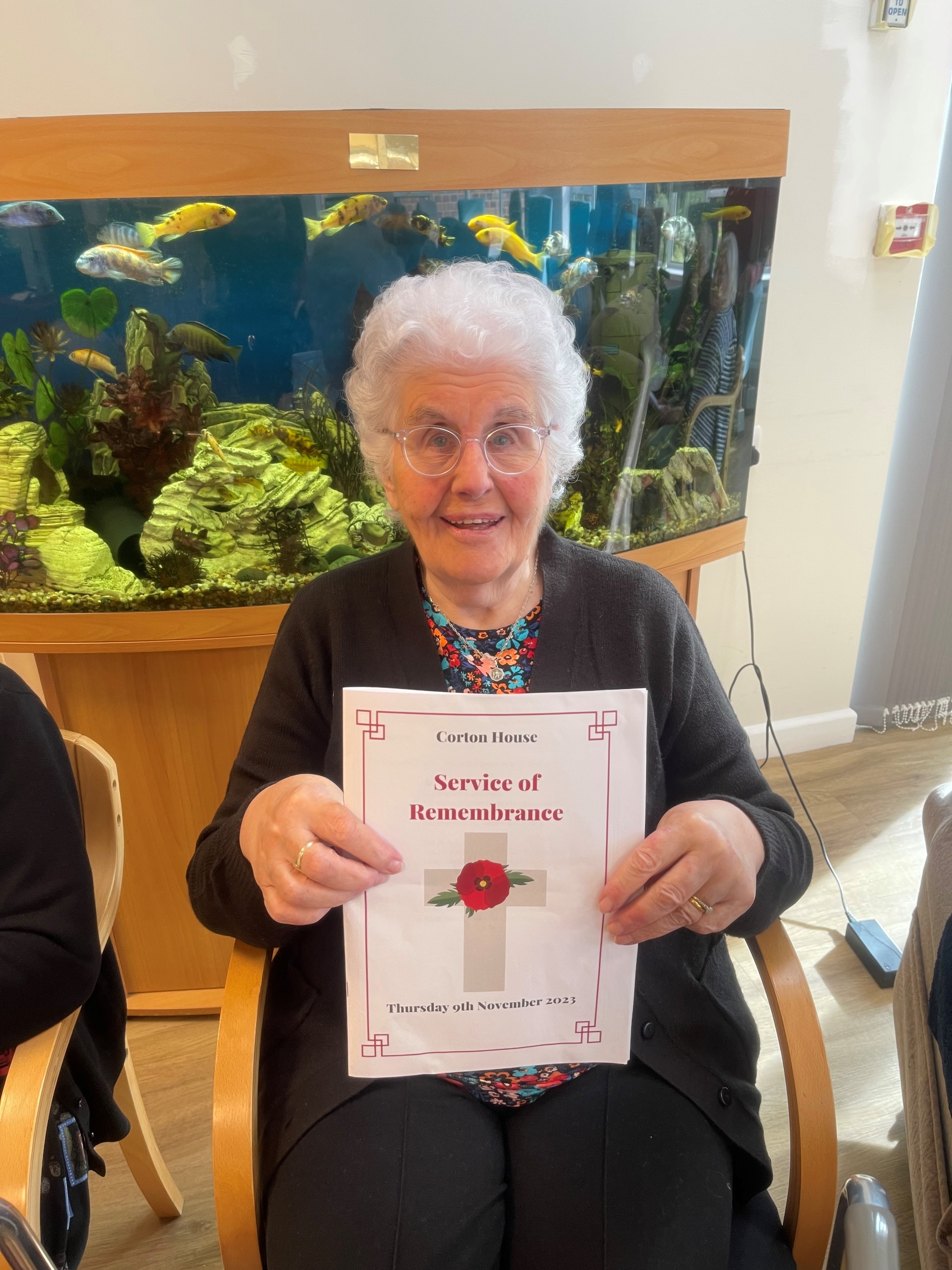 Norfolk Care Home resident Norma smiles and holds a Remembrance Service booklet