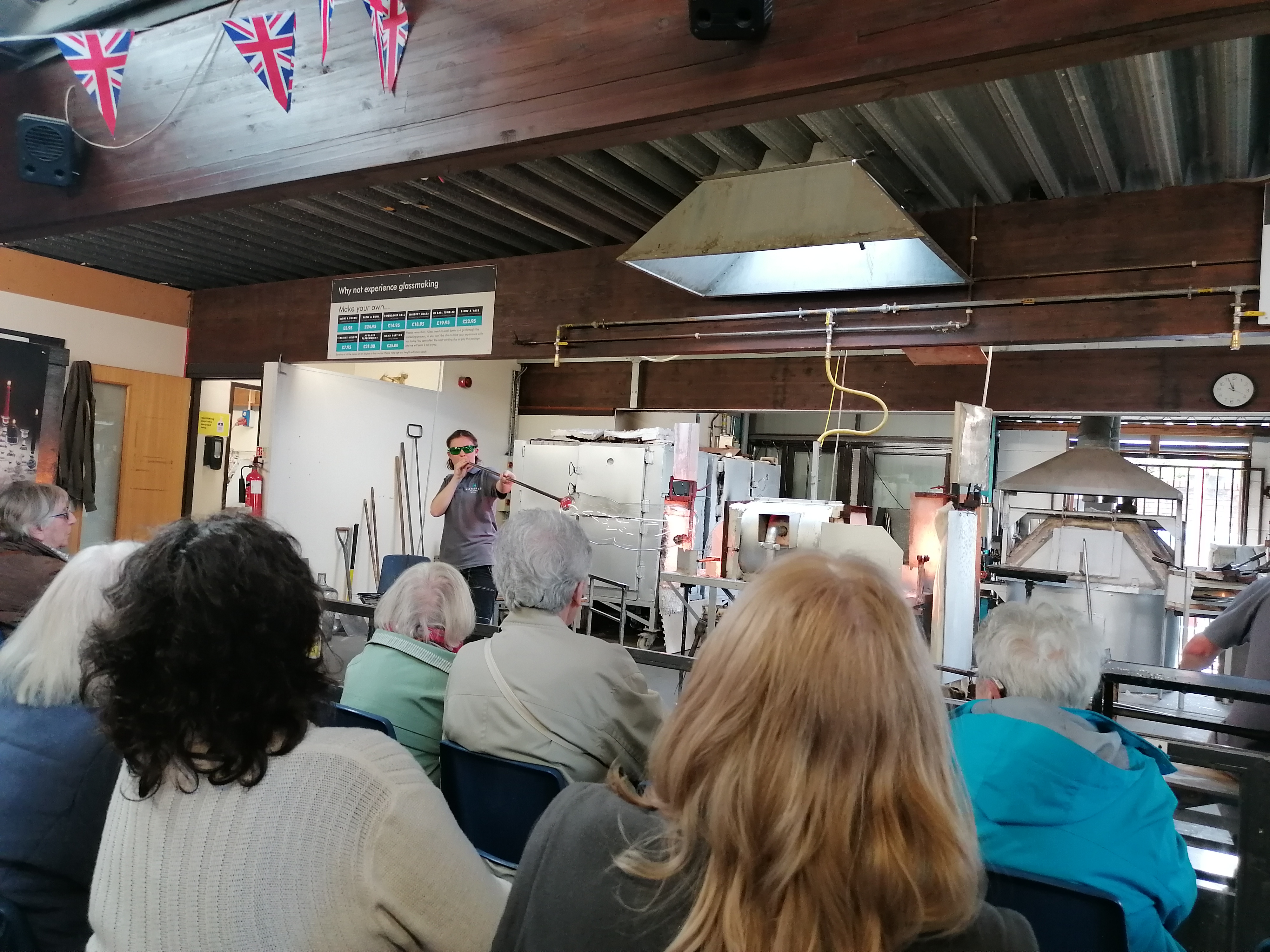 A glass maker blows a huge bubble of glass in front of a group of tenants.