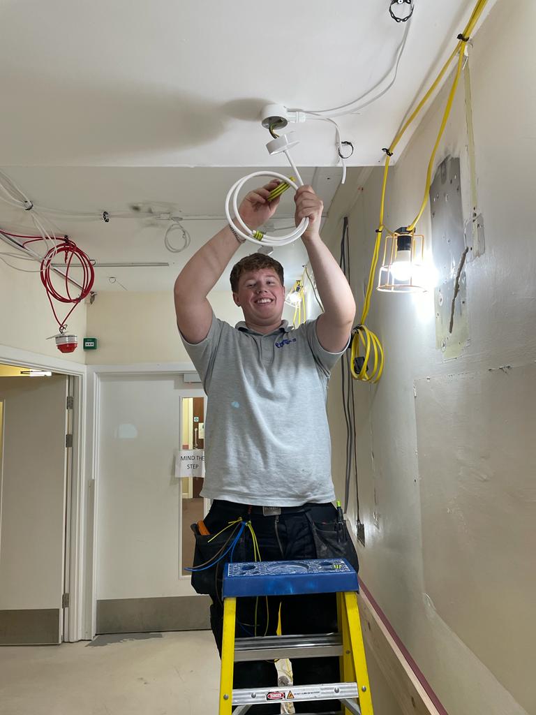 A tradesperson up a ladder wiring the ceiling