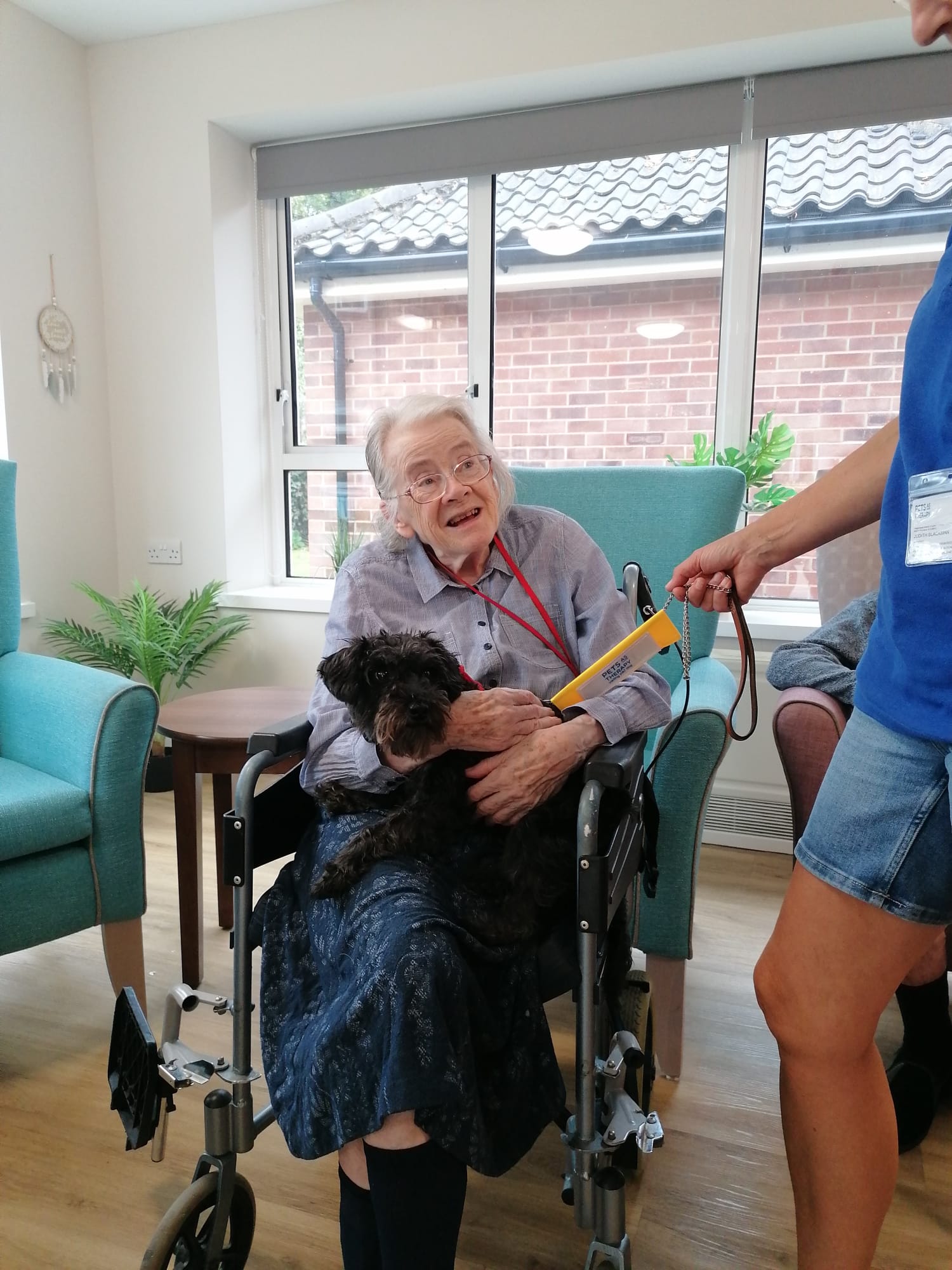 A resident holds a therapy dog on her lap and talks to its handler.