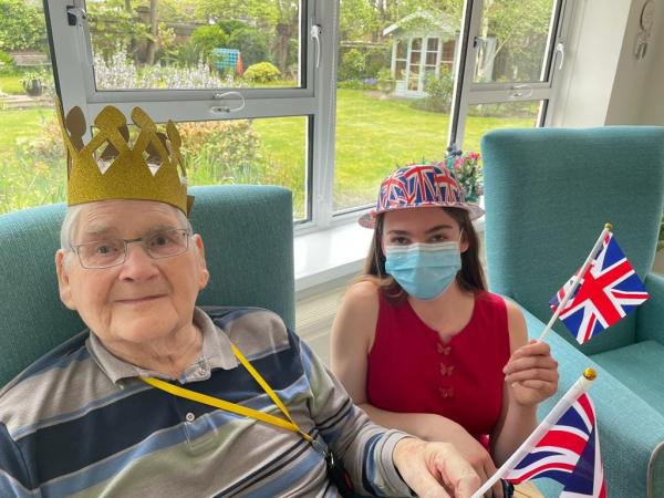 A smiling resident with a student volunteer, both wearing Coronation party hats.