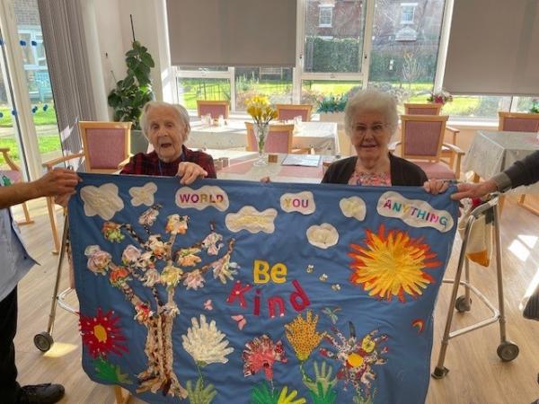 residents smile and hold textile art work created with local school children