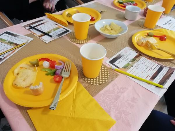 A table set with yellow paper plates and cups, and taste test score cards.