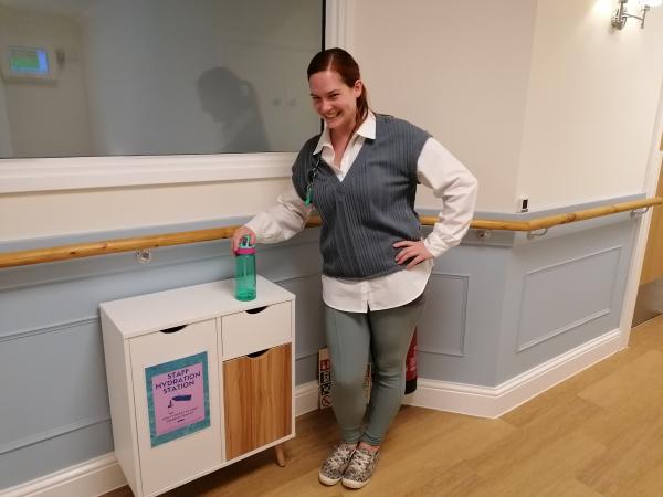 A smiling Corton House staff member with water bottle at a hydration station