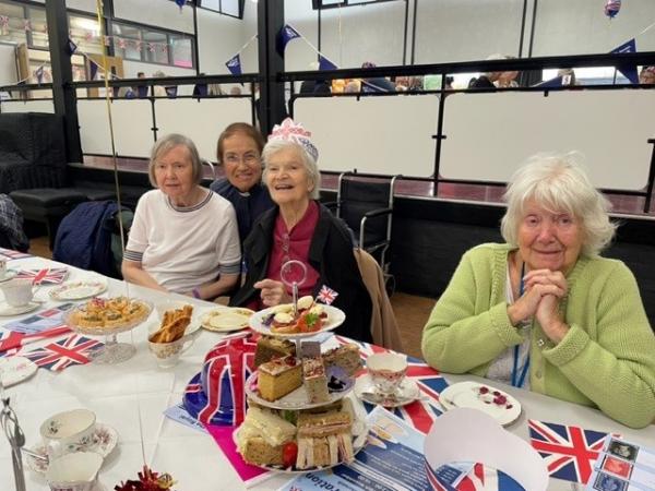 Flags and afternoon tea on a table before three smiling corton house residents