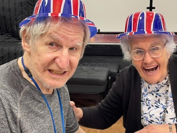 Two care home residents laughing and wearing union jack hats