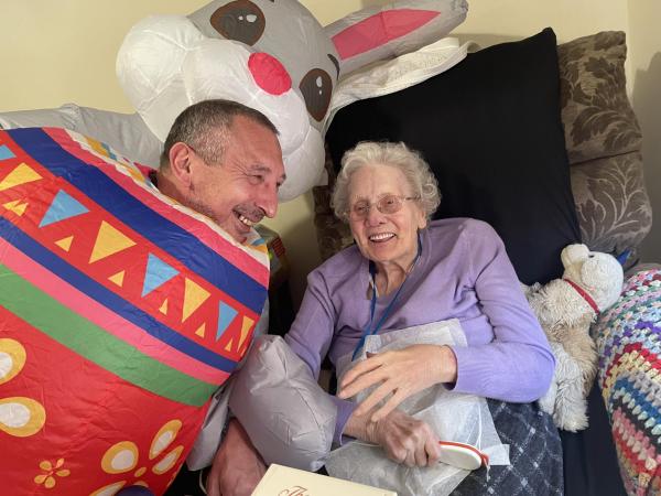 Manager dressed as the easter bunny visits a residenr, both are laughing