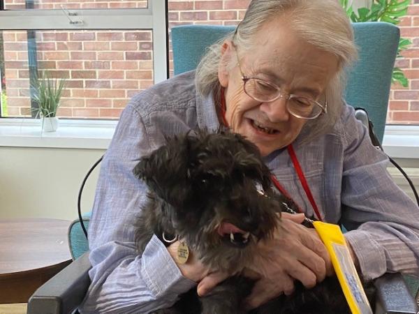 A smiling resident cuddles a therapy dog.