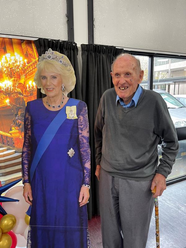 A care home resident smiles next to a cardboard figure of Queen Camilla