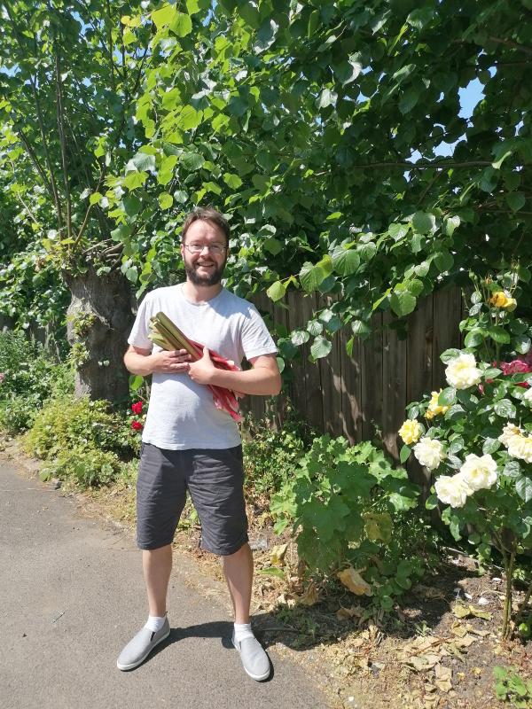 Staff member Rob smiling and holding a bunch of fresh rhubarb.