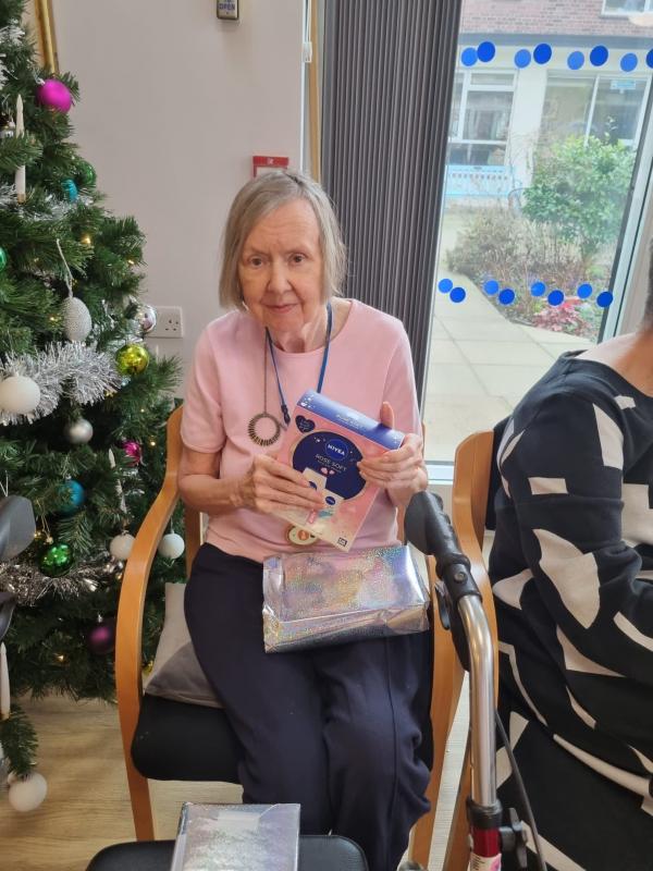 A resident opens a gift by the Christmas tree in Corton House care home