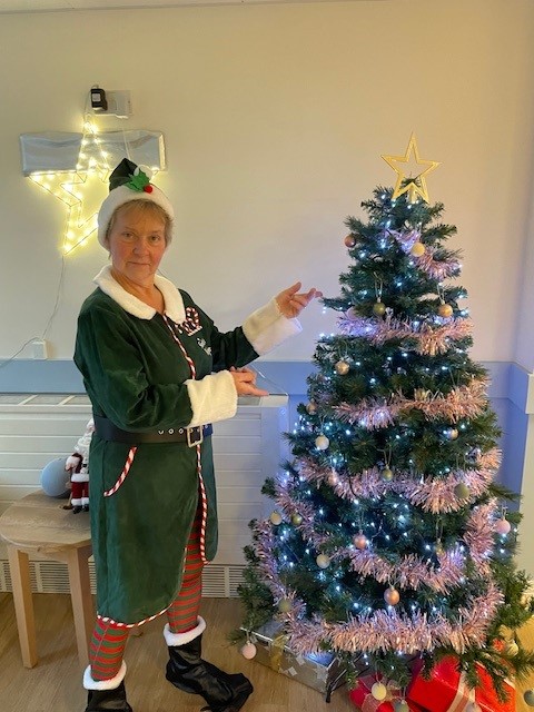 A staff member dressed as an elf stands next to a Christmas tree in the foyer