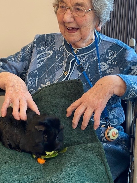 a smiling resident with a black fluffy guinea pig on her lap