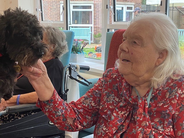 A resident smiles at a therapy dog held in front of her.