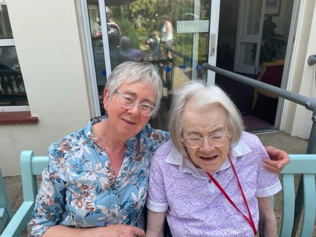 Resident and daughter on a green bench on the patio.