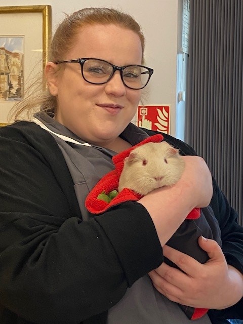 a staff member cuddles a guinea pig and smiles