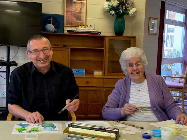 Manager Jason laughs alongside a Corton House resident. Both are painting.