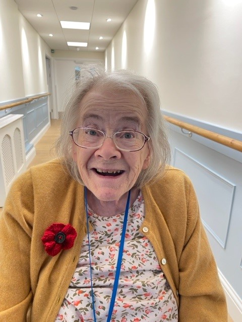 A smiling resident in Norwich care home Corton House wears a poppy