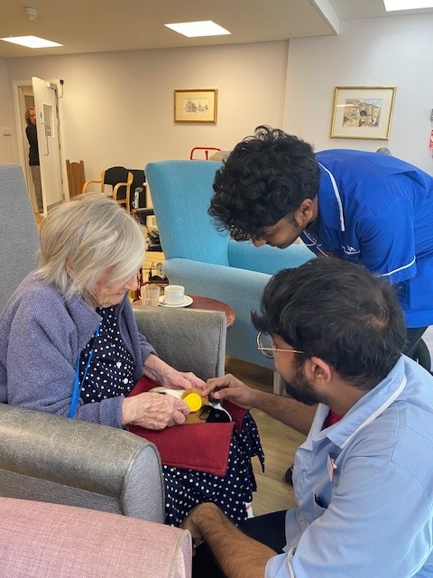 a resident is supported by care assistants to pet a visiting therapy animal 
