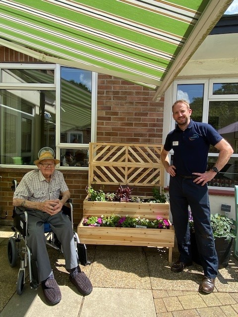 A resident and volunteer smile next to a newly built planter filled with flowers