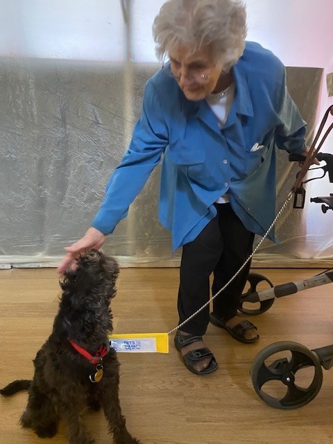 A resident stands with a walker and pets a therapy dog.